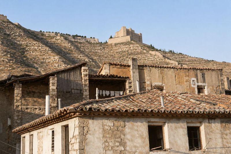Tejados de teja árabe y fachadas gastadas, con una galería de cañizo y ropa tendida; detrás, el cerro con cipreses y el castillo.