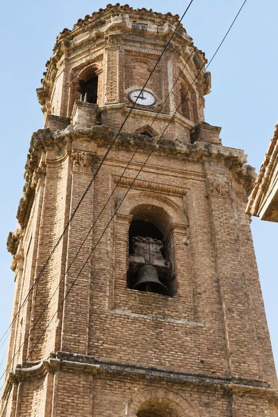Primer plano de la torre de ladrillo, con el campanario, el reloj en el cuerpo octogonal superior y cables que cruzan la fachada.