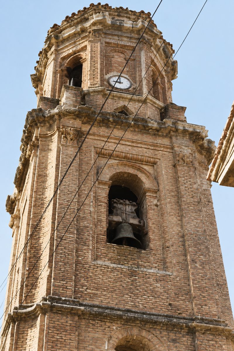 Primer plano de la torre de ladrillo, con el campanario, el reloj en el cuerpo octogonal superior y cables que cruzan la fachada.