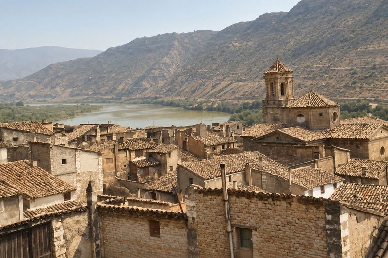 Tejados de teja y la iglesia con cimborrio y torre, vistos desde una parte alta; detrás, el río en una curva y montañas.