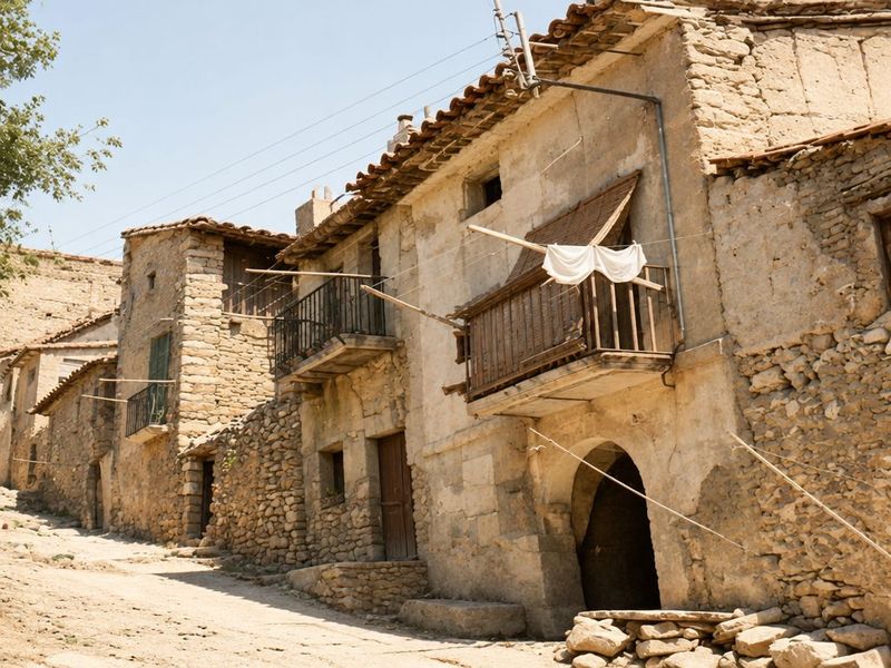 Fachadas de mampostería con revoco caído y alero de teja; un balcón de madera con ropa tendida sobre un portal de medio punto, y cuerdas cruzando la calle.