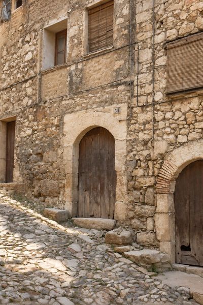 Portal de medio punto con dovelas y puerta de madera, con el número 51 sobre el arco, en una fachada de mampostería sobre una calle de canto rodado en cuesta.
