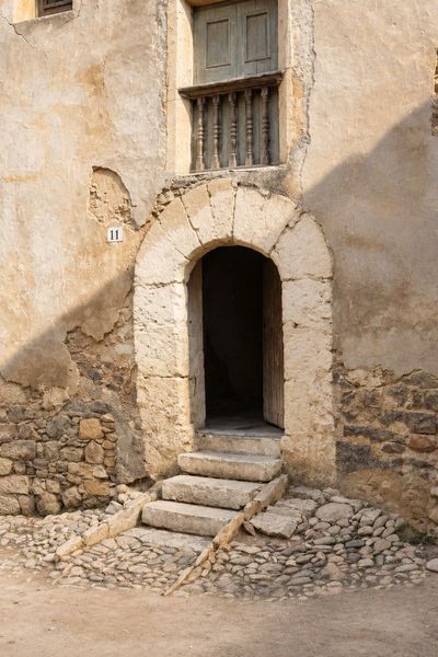 Portal de arco de medio punto con dovelas y tres escalones sobre un empedrado, con una puerta de madera entreabierta, un balcón de balaustres arriba y una placa con el 11.