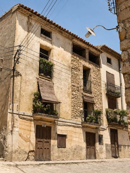 Tres fachadas contiguas: una encalada con balcones y toldo de caña, otra de mampostería vista y otra encalada, con una farola de brazo y cables sobre la calle.