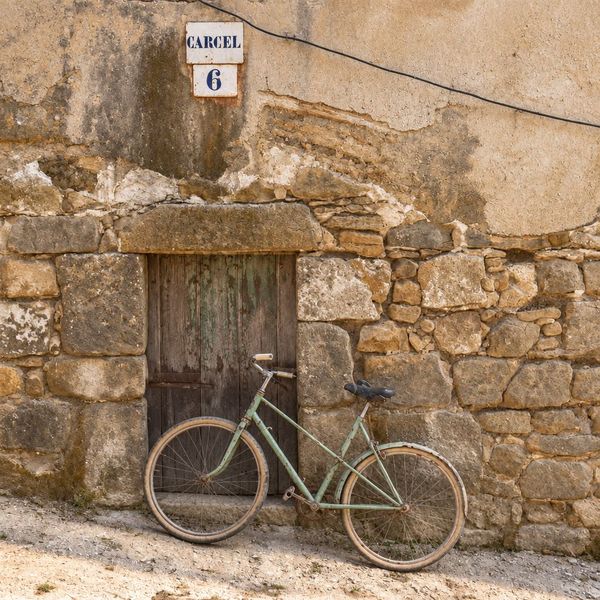 Fachada de la «presó» con la placa «CARCEL 6» sobre un muro de grandes piedras, una puerta de madera y una bicicleta apoyada.
