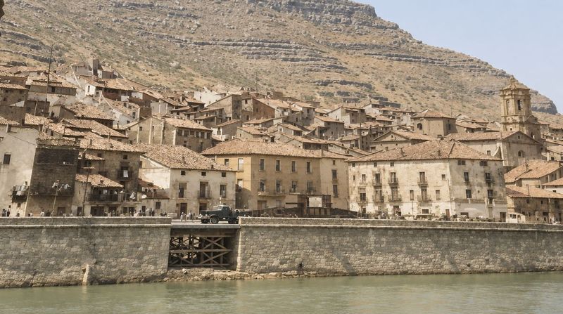 El frente del muro con un paso reforzado con puntales de madera; detrás, casas de varias plantas, la iglesia con su torre a la derecha y el cerro, con gente a lo largo de la calle.
